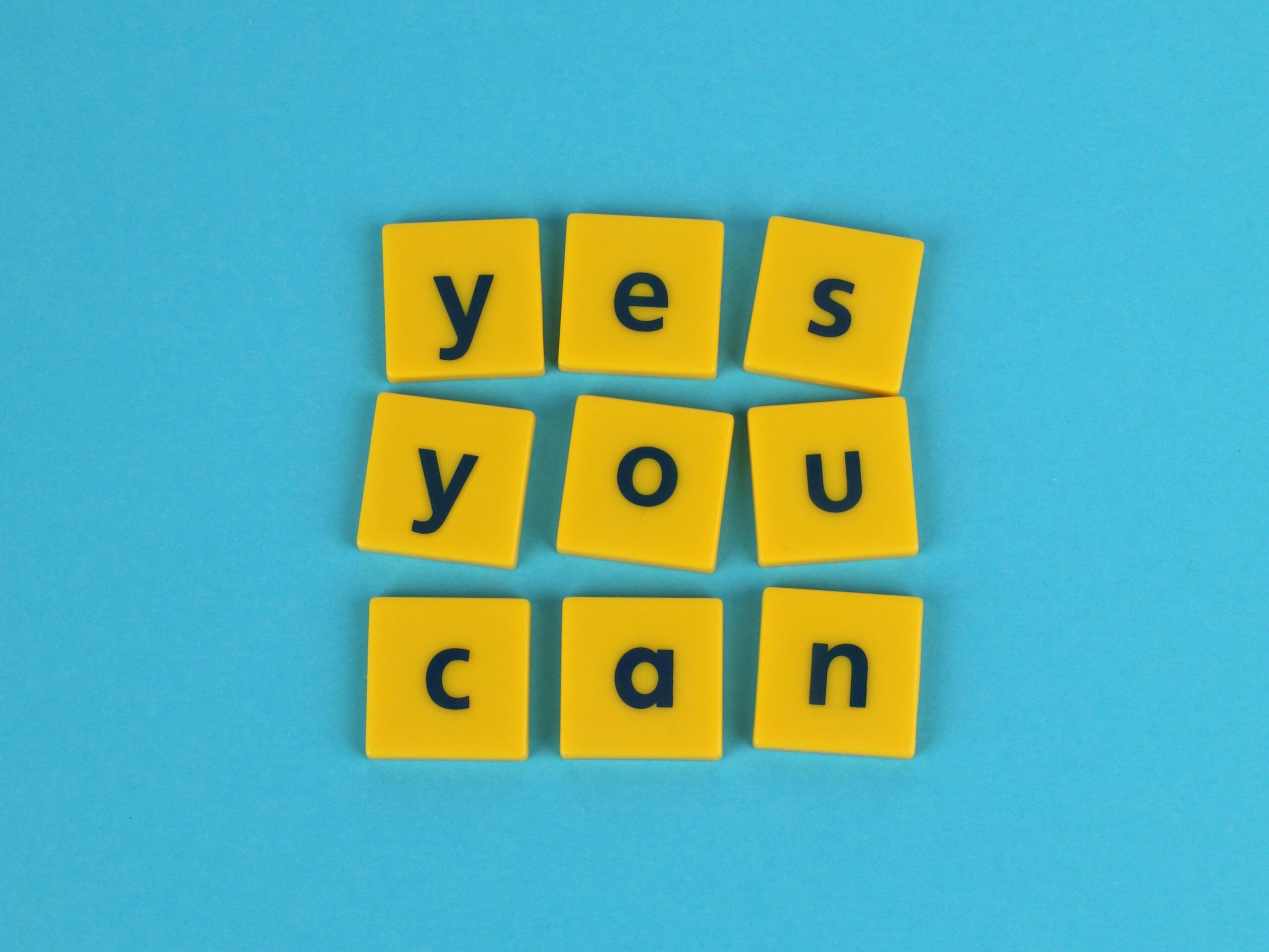 Yellow tiles on blue background spelling 'yes you can', promoting motivation and positivity.