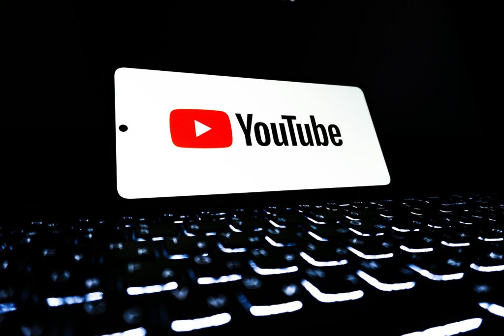 YouTube app icon displayed on a smartphone over an illuminated keyboard, representing digital media and online streaming. YouTube