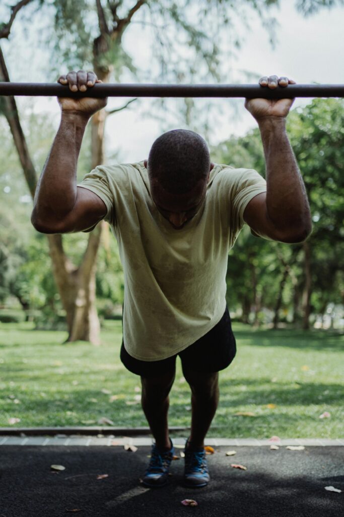 A man performs an exercise using an iron bar in an outdoor park setting during the day. Physical Exersize