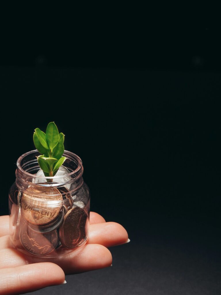 A small plant growing in a glass jar filled with coins, represents financial growth and sustainability. Saving vs Investing 