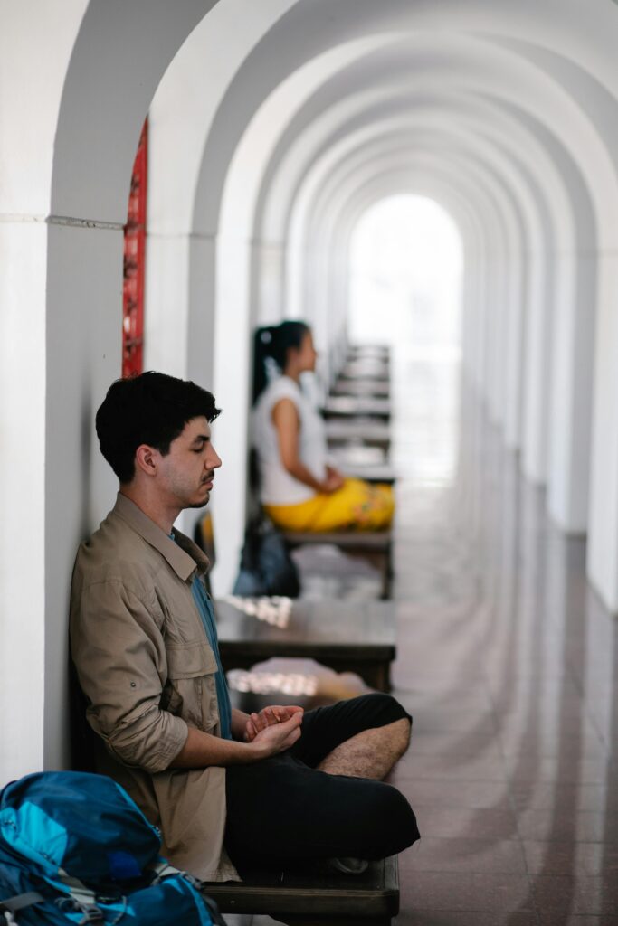 Man meditating with eyes closed in a serene arched hallway, embodying peace and mindfulness.
