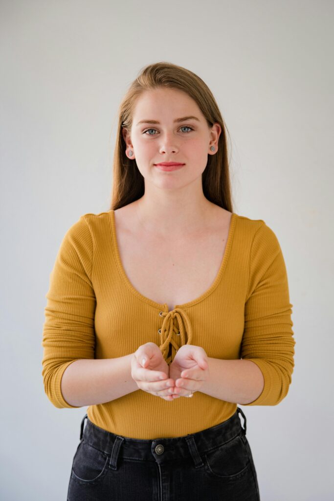 Portrait of a young Caucasian woman in yellow top using sign language against a plain background.
Body Language 