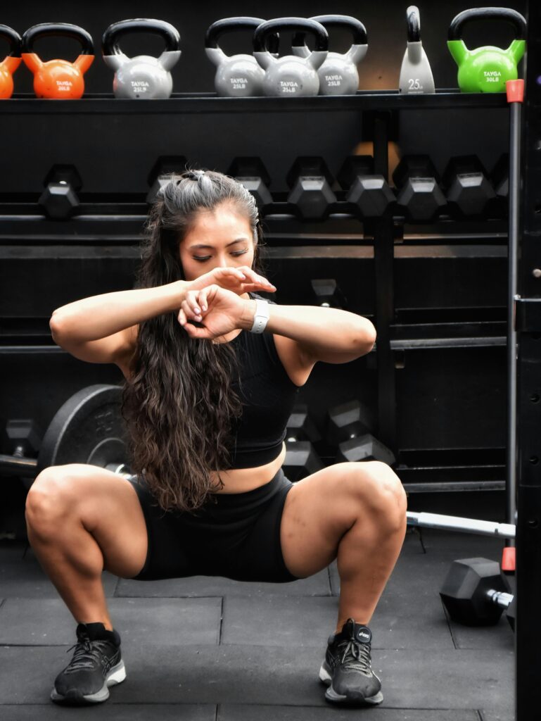 Focused woman squatting in a gym setting surrounded by kettlebells, showcasing determination and fitness.