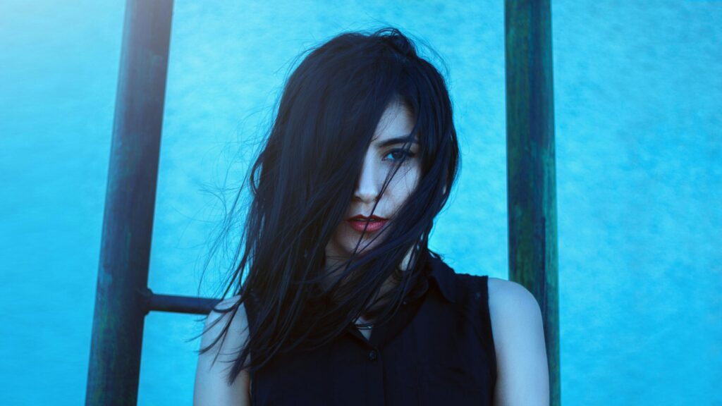 A striking portrait of a woman with flowing hair set against a vibrant blue background.