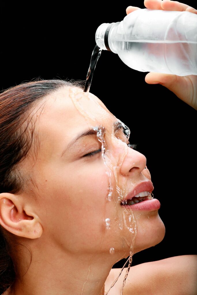 Close-up of a woman pouring water on her face against black background.