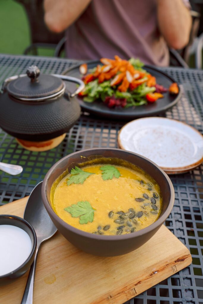 Delicious pumpkin soup with parsley and seeds served outdoors alongside a colorful salad.