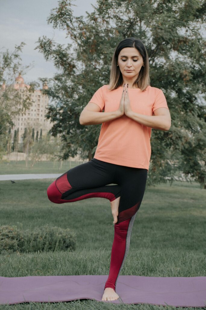 A woman in activewear practices yoga outdoors, performing the tree pose on grass.
Yoga Ka Importance