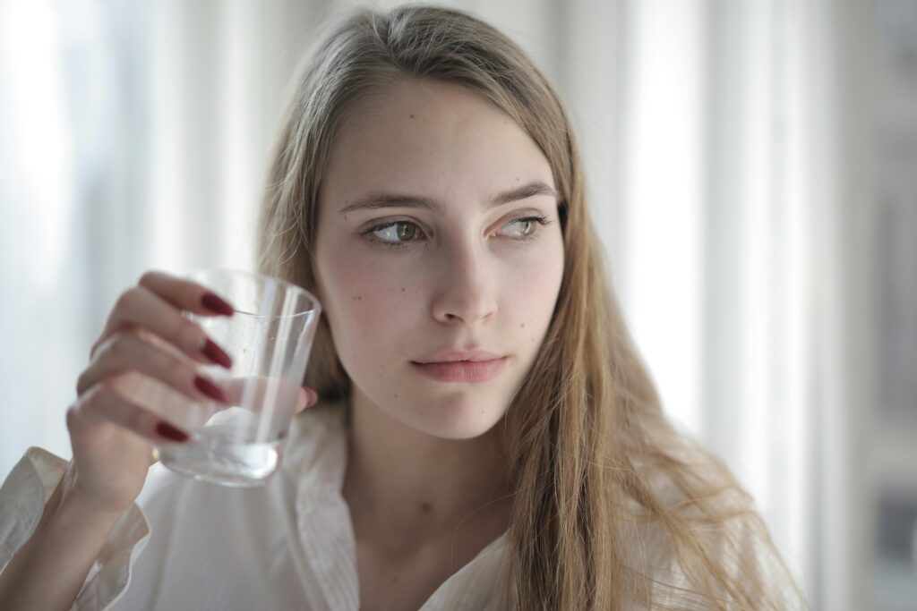 Young woman with long hair holding a glass of water, looking thoughtful.