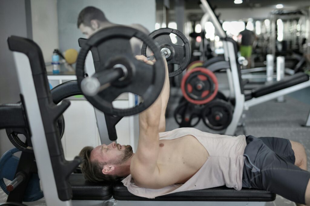Side view of strong young sportsman in sportswear lying on bench and pressing heavy barbell doing chest exercise training in modern gym