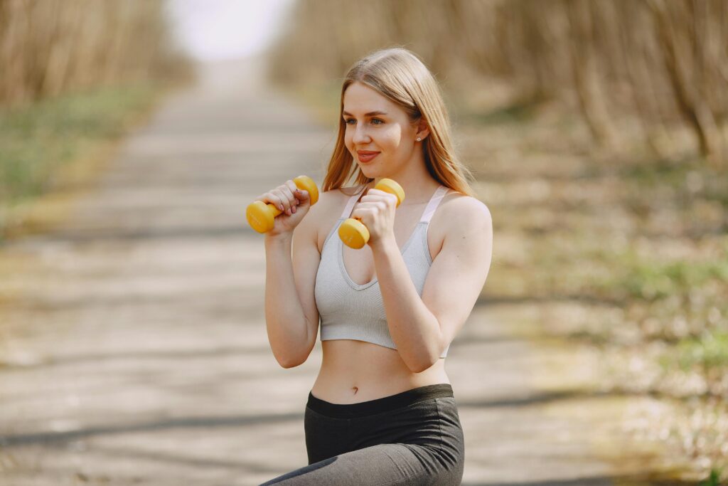 Fit woman lifting dumbbells on a sunny day, embracing a healthy outdoor workout.