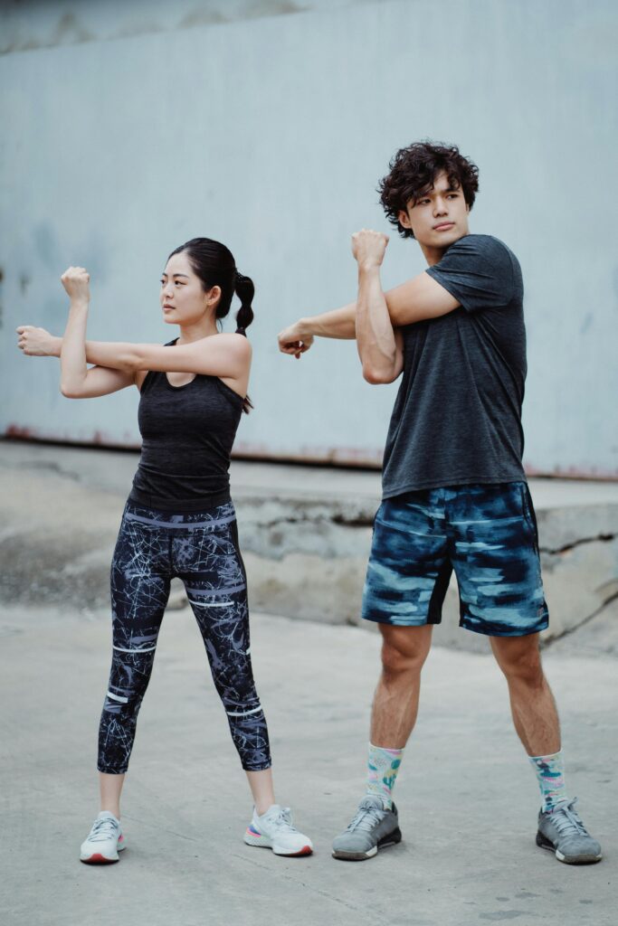 A young couple performing arm stretches outdoors, preparing for a workout.