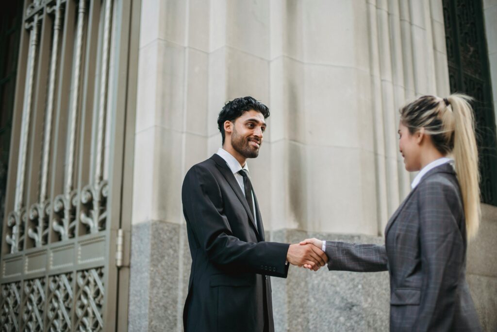 Two business professionals in formal attire shaking hands outside an elegant building, signifying partnership.
Logon Ko Impress Kaise Kare