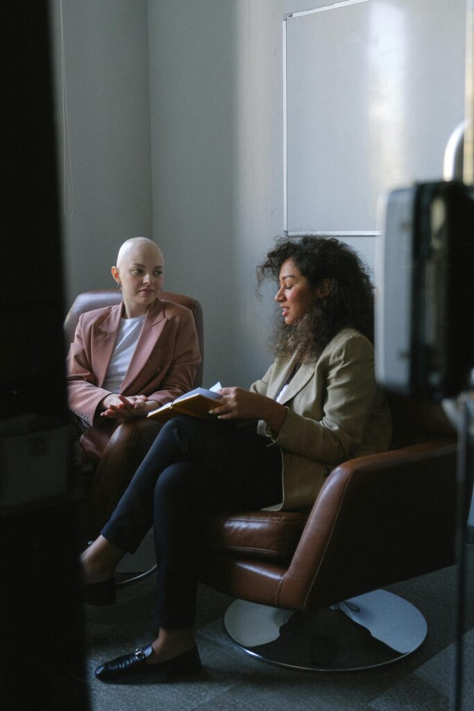 Positive African American lady sitting with copybook in conference hall and communicating with colleague in daytime