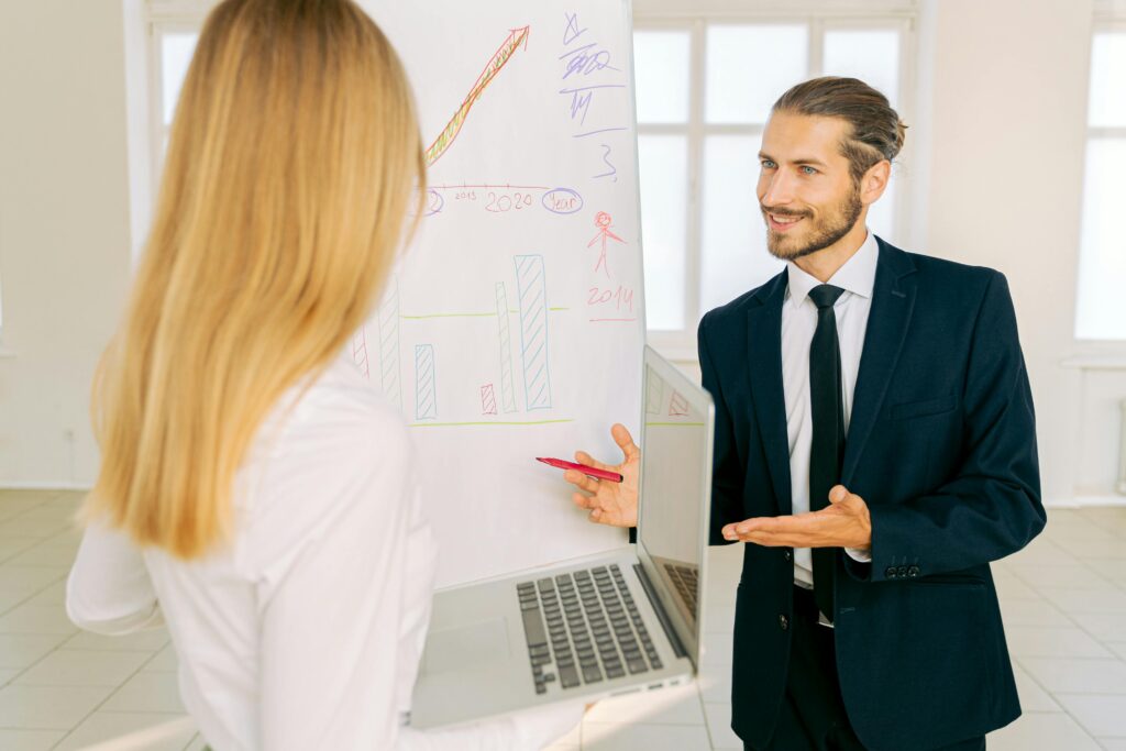 Two colleagues discussing a presentation on a whiteboard in a modern office setting.