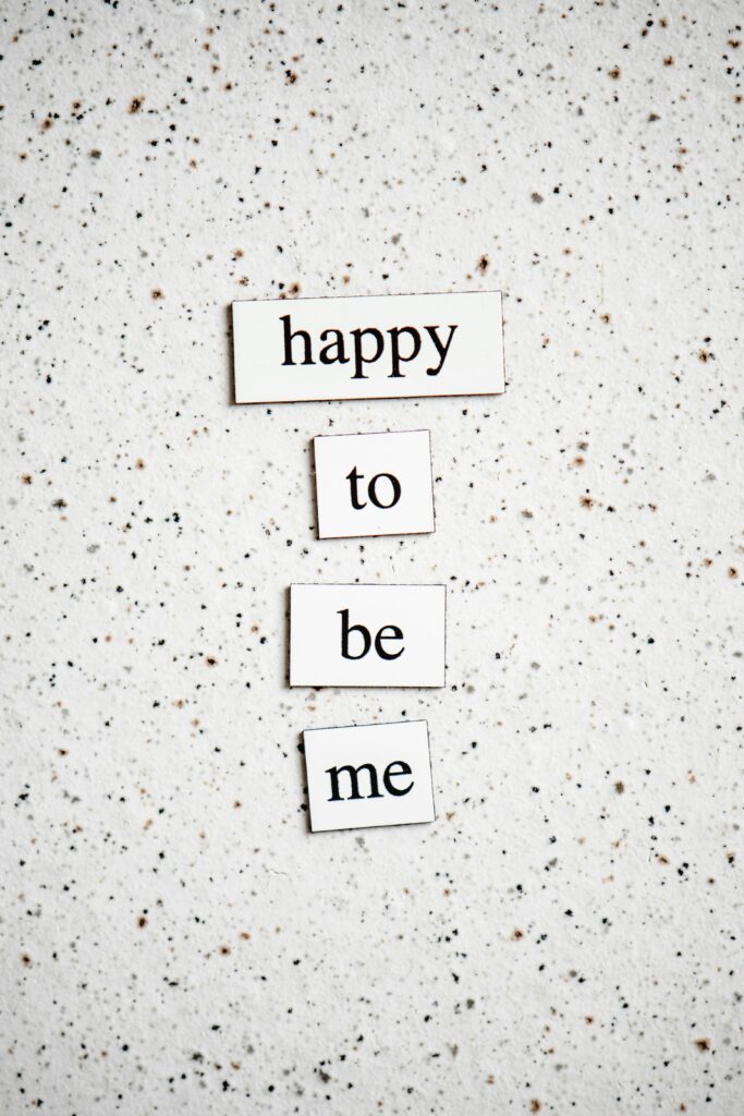 Inspirational typography message 'Happy to be me' on a speckled surface, promoting positivity.