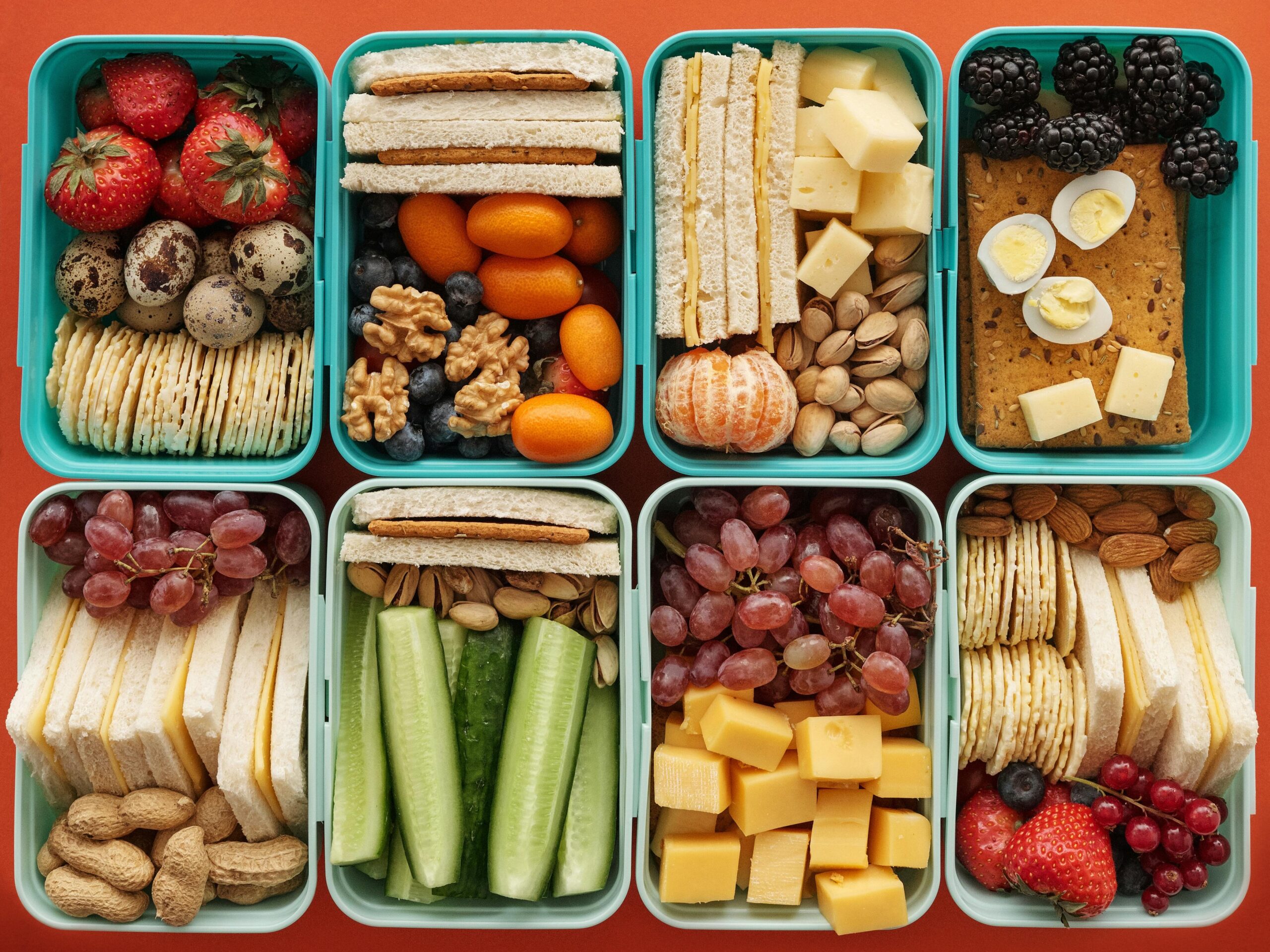 Top view of diverse snack boxes arranged neatly on an orange backdrop, ideal for meal prep inspiration.