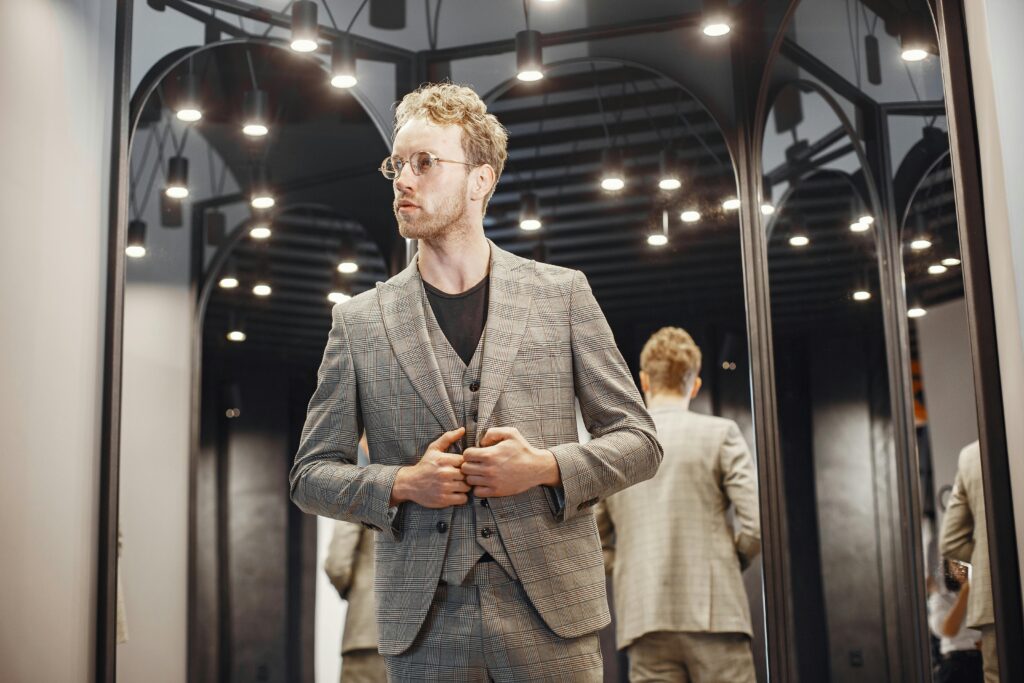 Elegant young man adjusts his suit in a well-lit dressing room. Fashion and style concept.