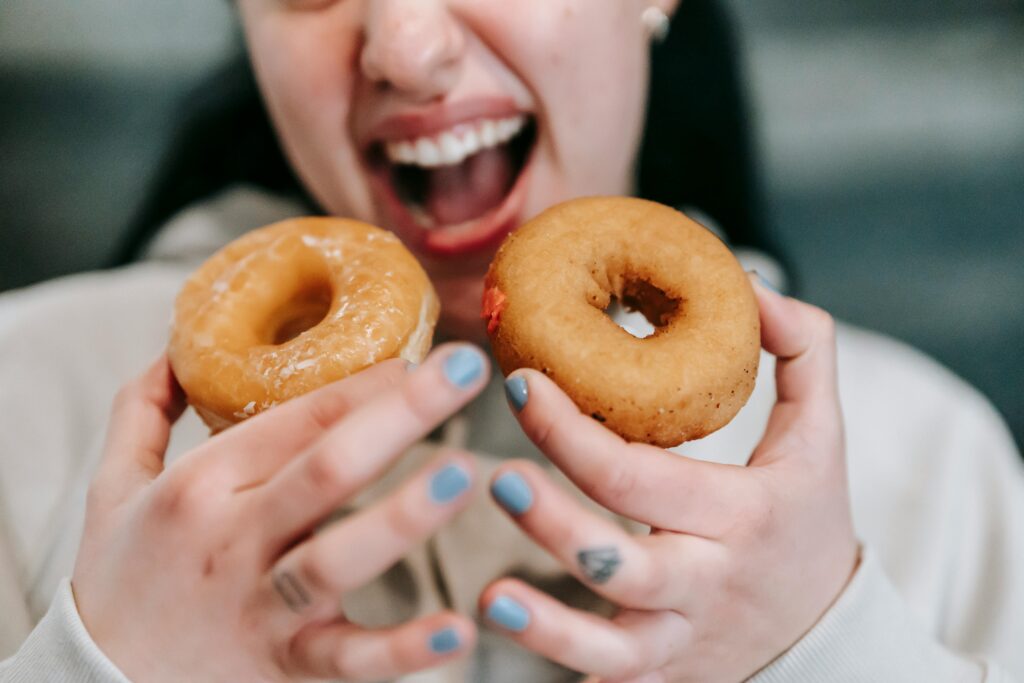 Crop expressive brunette wearing casual outfit opening mouth to bite tasty sweet doughnuts in studio