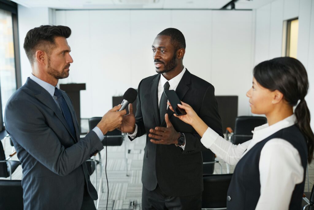 African American businessman in formal attire being interviewed by journalists with microphones in a conference room. Communication Skills