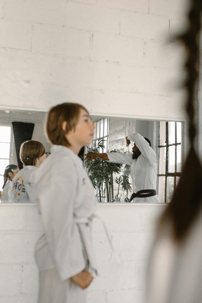 Karate students practice in a studio, reflecting in a wall mirror during training session.