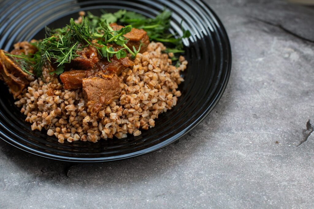Delicious buckwheat with seasoned beef and greens served on a black plate.