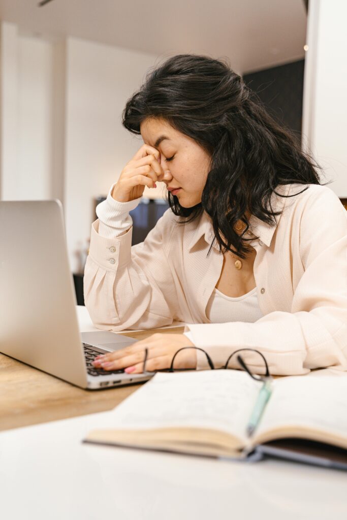 Woman with closed eyes feeling frustration while working on a laptop indoors.