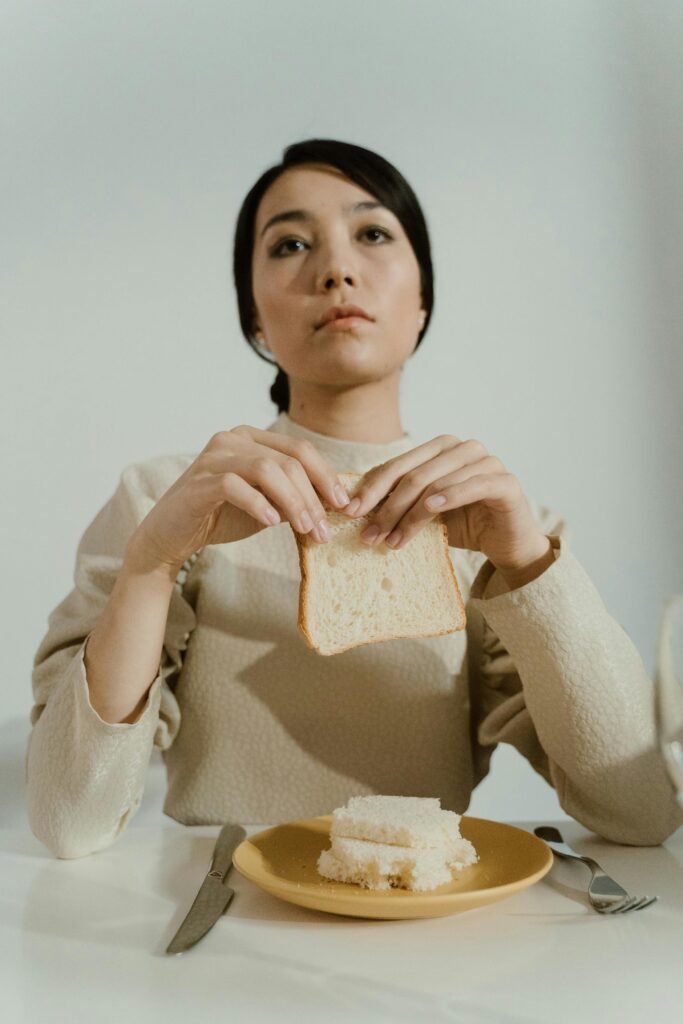 A woman sits at a table holding bread, evoking a contemplative mood.