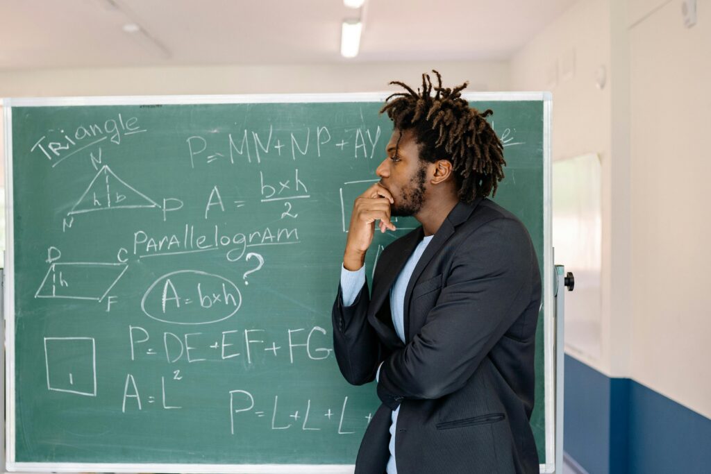 Teacher contemplating in front of a chalkboard with math equations.
English Bolna Kaise Improve Kare