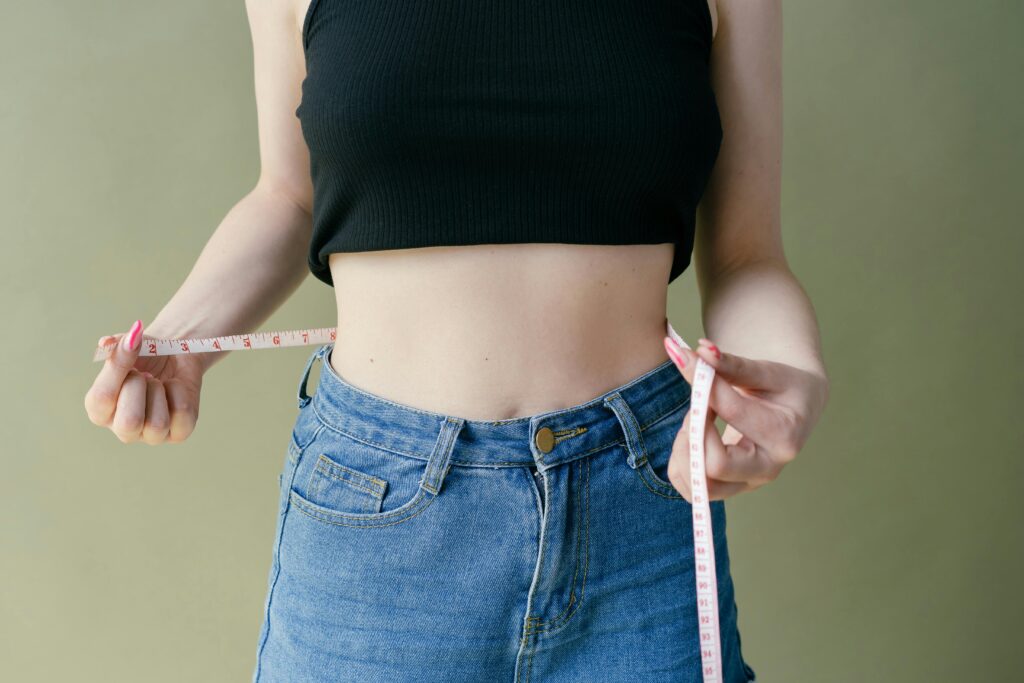 A woman in denim and crop top using measuring tape for waist check.