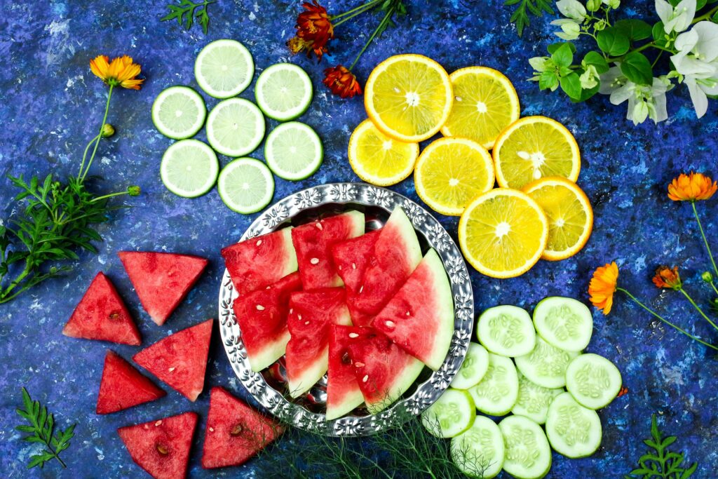 Colorful flat lay of watermelon, citrus, cucumber slices, and flowers on a blue background.
