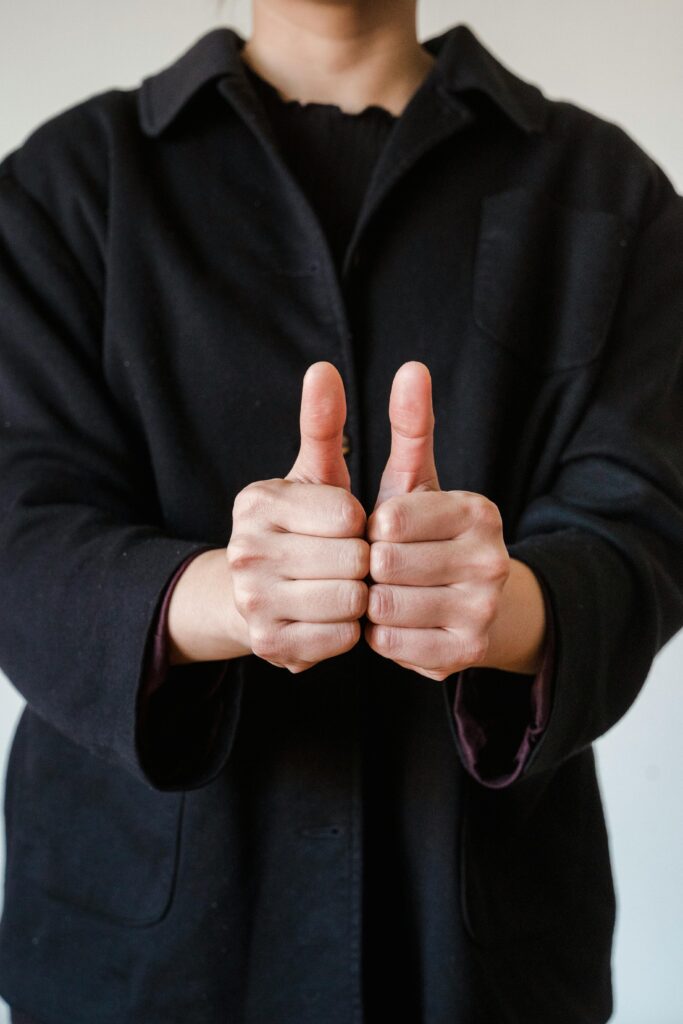 Close-up of person giving a double thumbs up sign in a black jacket, symbolizing approval.