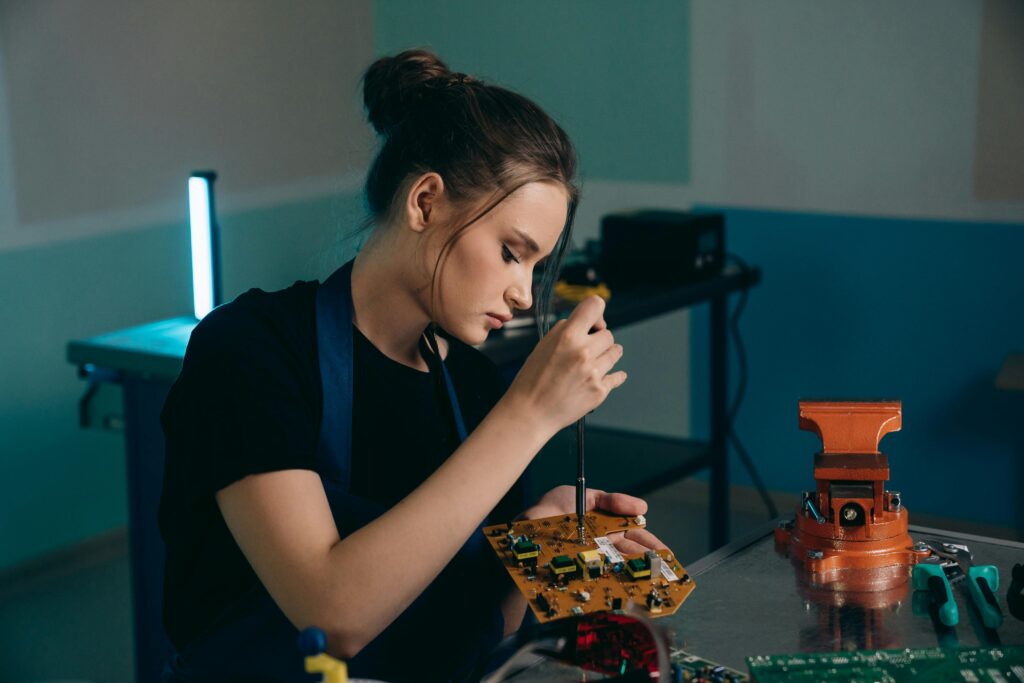 Focused young woman assembling electronics in a workshop setting.