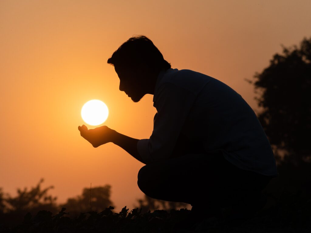 Silhouette of a man crouching, holding the sun during sunset, creating a serene and artistic scene.