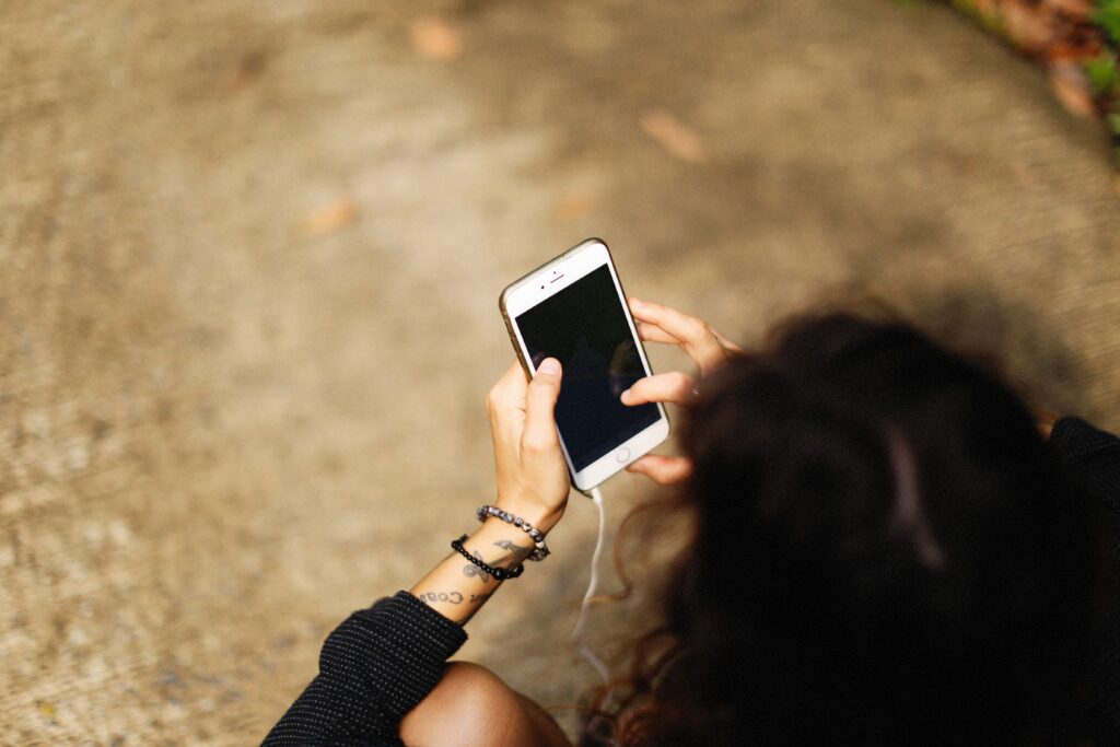 High-angle view of a young woman holding a smartphone outdoors, focusing on her hands and device.