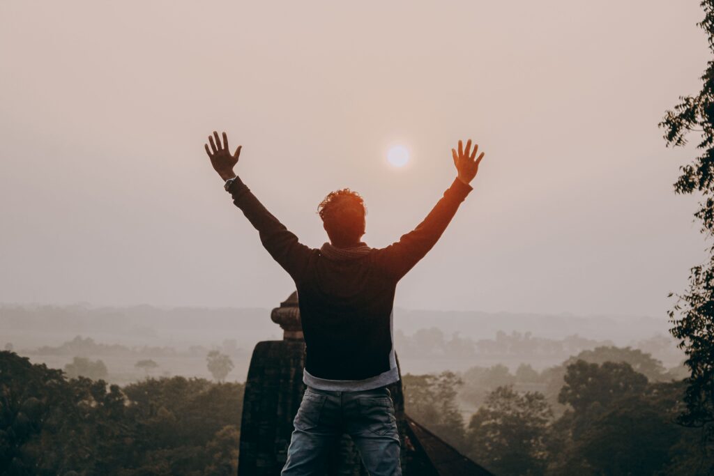 A man with outstretched arms stands against a sunrise in Odisha, India, symbolizing freedom and serenity.