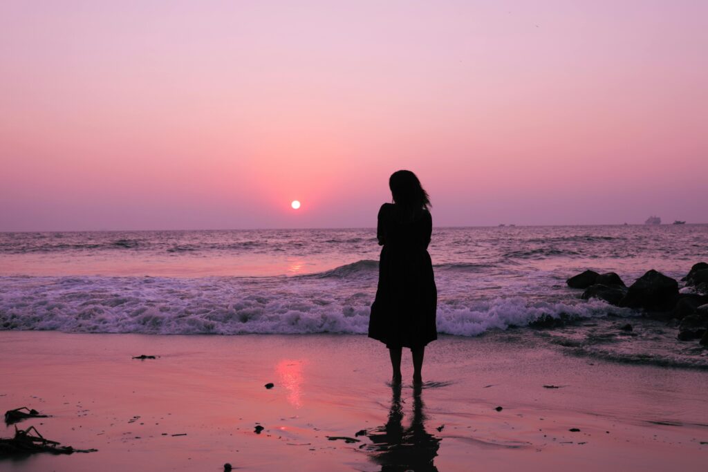 A tranquil scene of a woman silhouetted against the vibrant sunset over the ocean waves.