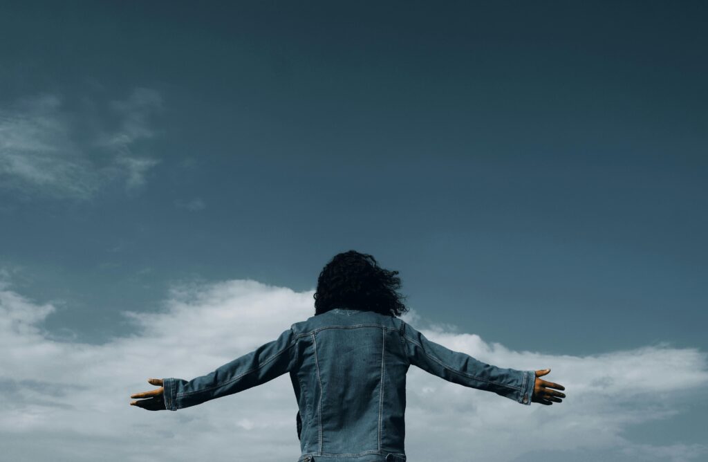 A woman with arms outstretched stands against a dramatic sky, symbolizing freedom and exploration.