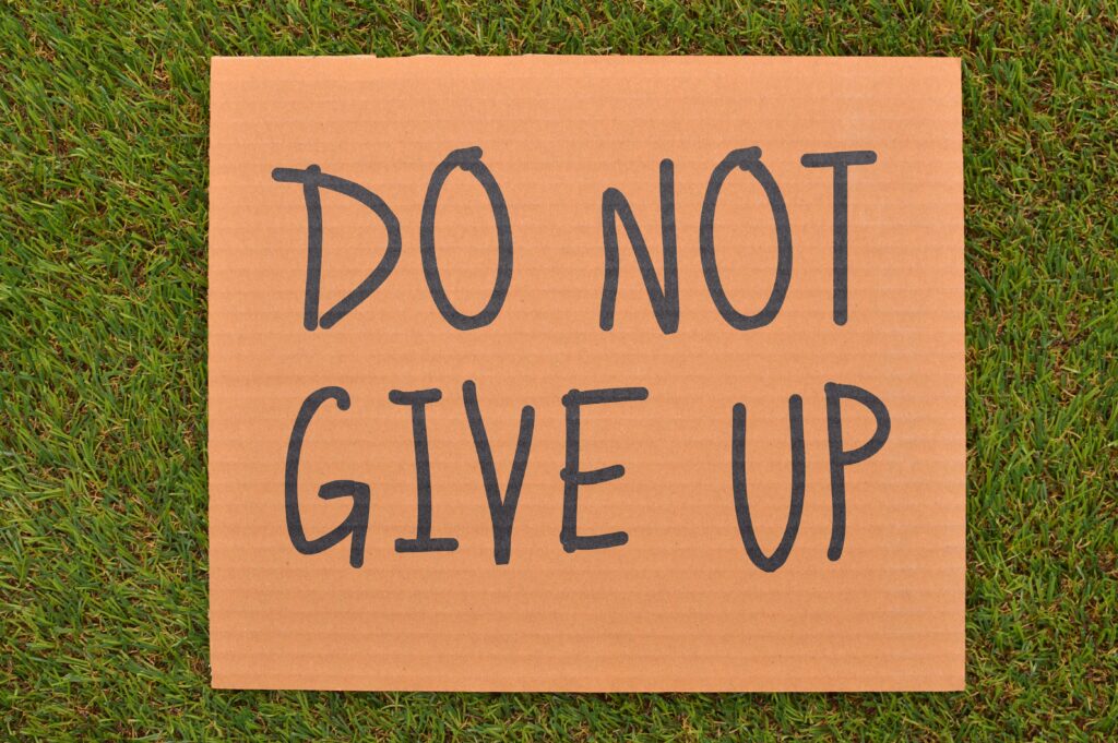 Cardboard sign reading 'Do Not Give Up' placed on green turf, symbolizing perseverance.
Never Give Up Mindset Kaise Banaye 