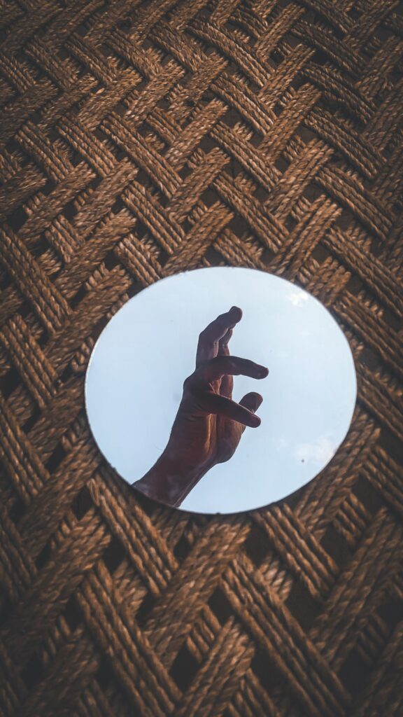 A creative shot of a hand reflecting in a circular mirror on a woven background.