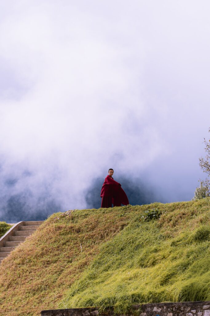 A solitary Buddhist monk stands on a grassy hill with misty mountains in Dirang.