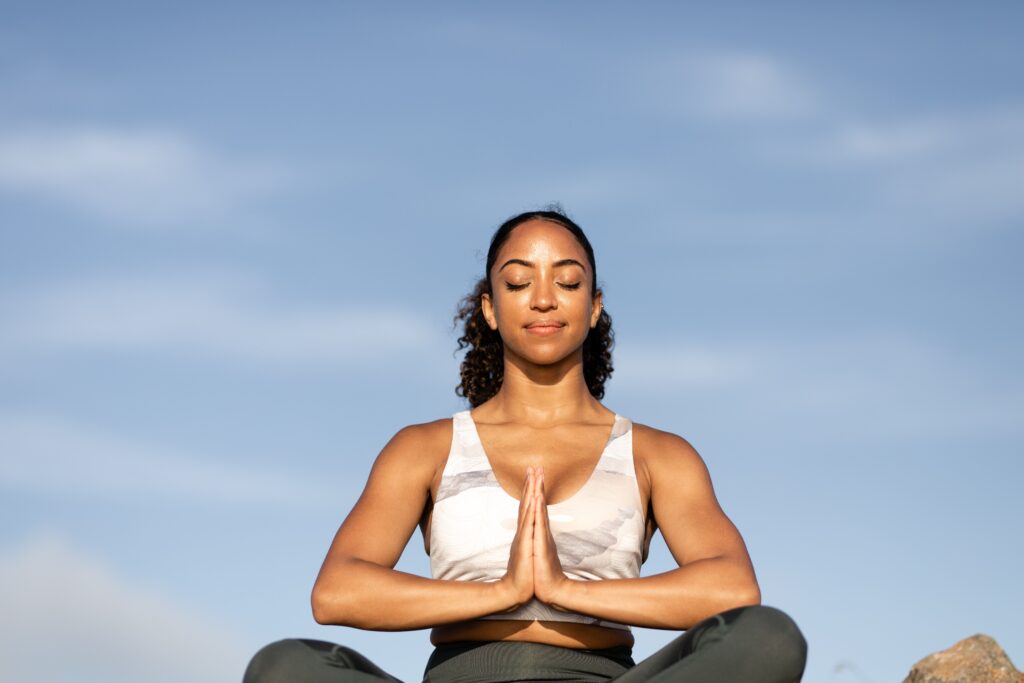 A woman meditating outdoors with eyes closed under a blue sky, embracing peace and mindfulness.