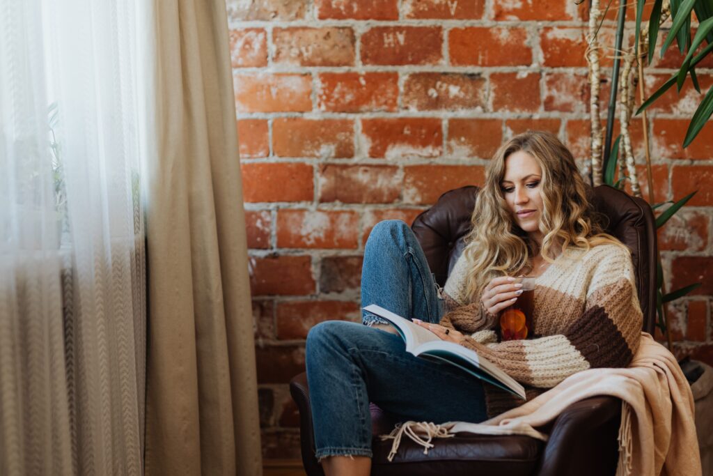 Woman relaxing with a book and tea in a cozy setting by a brick wall.