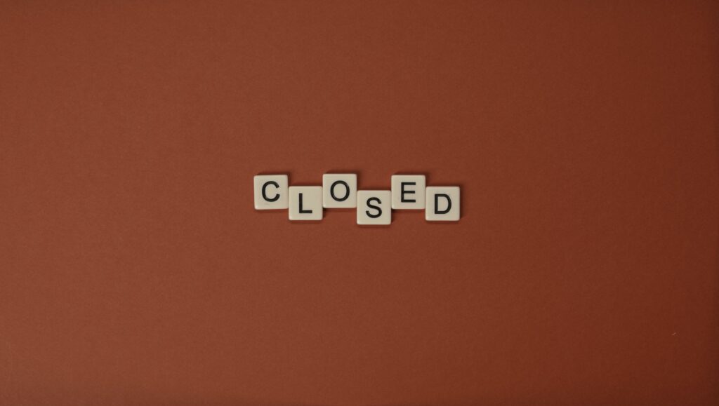 Scrabble letter tiles spelling 'CLOSED' on a brown background, minimalist design.