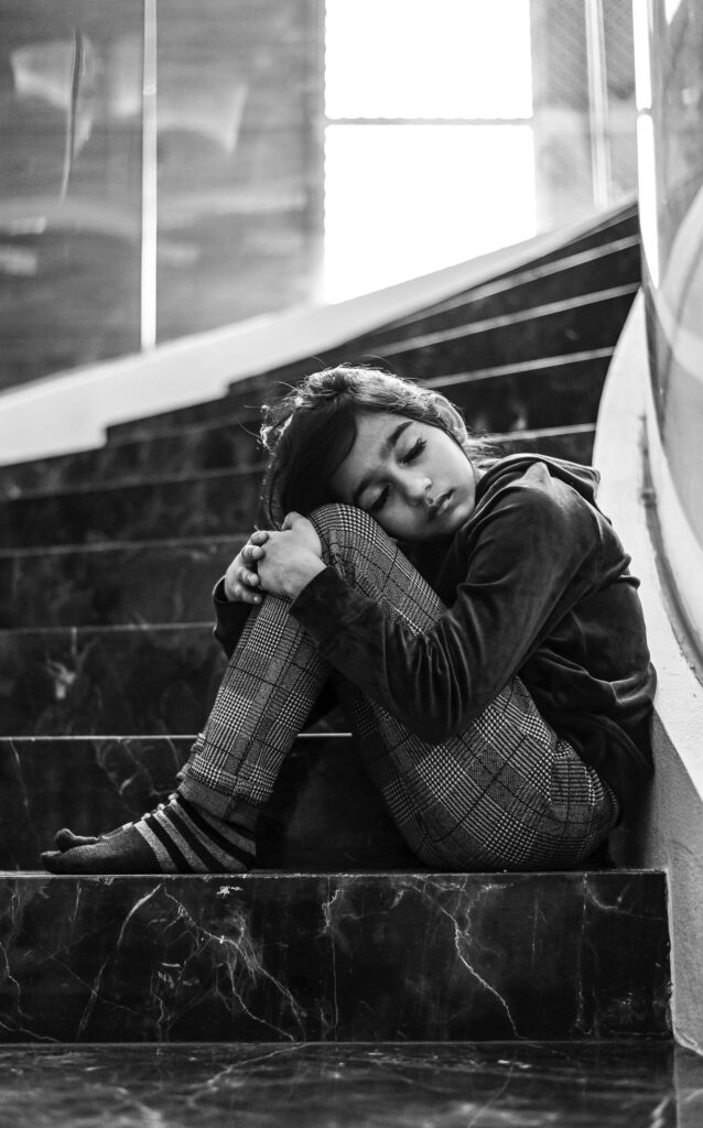 Black and white photo of a child sitting on stairs, appearing lonely and upset.