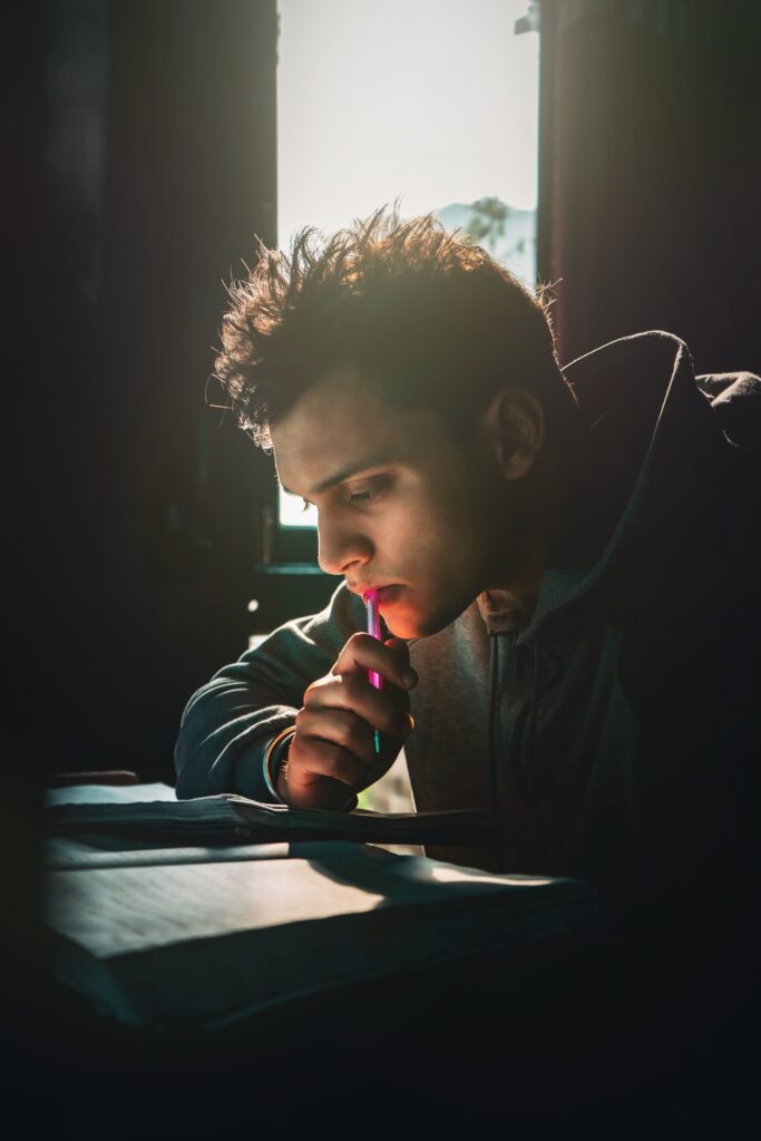 A young man intensely studying indoors, lit by sunlight from a window.