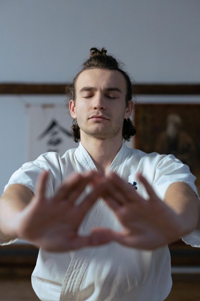 A man in martial arts attire meditates indoors, focusing on mindfulness and tranquility.