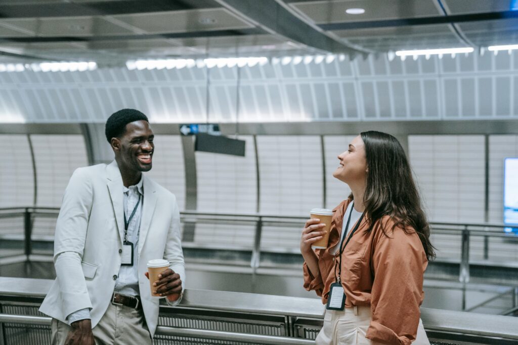 Two professionals chat warmly over coffee in a sleek, modern building setting.