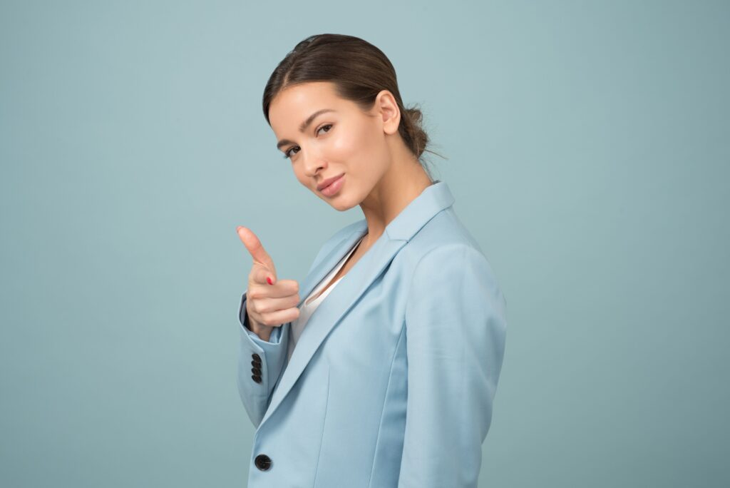 A young woman in a blue suit exhibits confidence with a relaxed pose against a blue background.