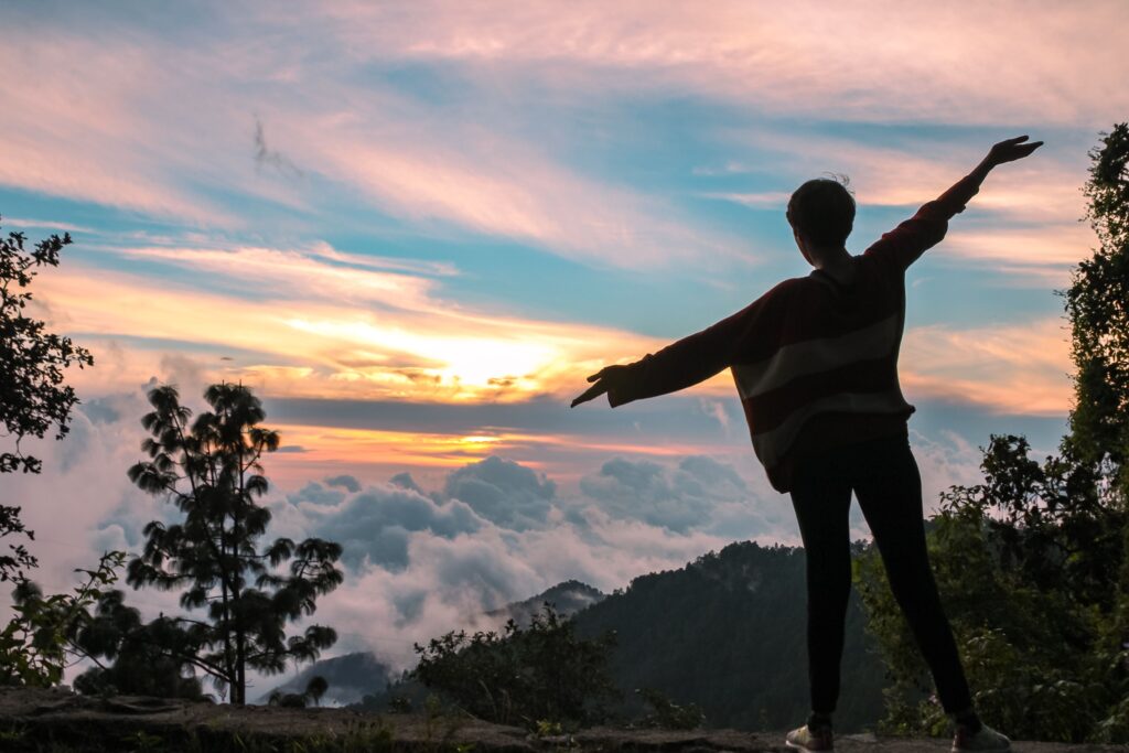 A person silhouetted against a breathtaking sunset over mountains and clouds at El Pacífico, Oaxaca.