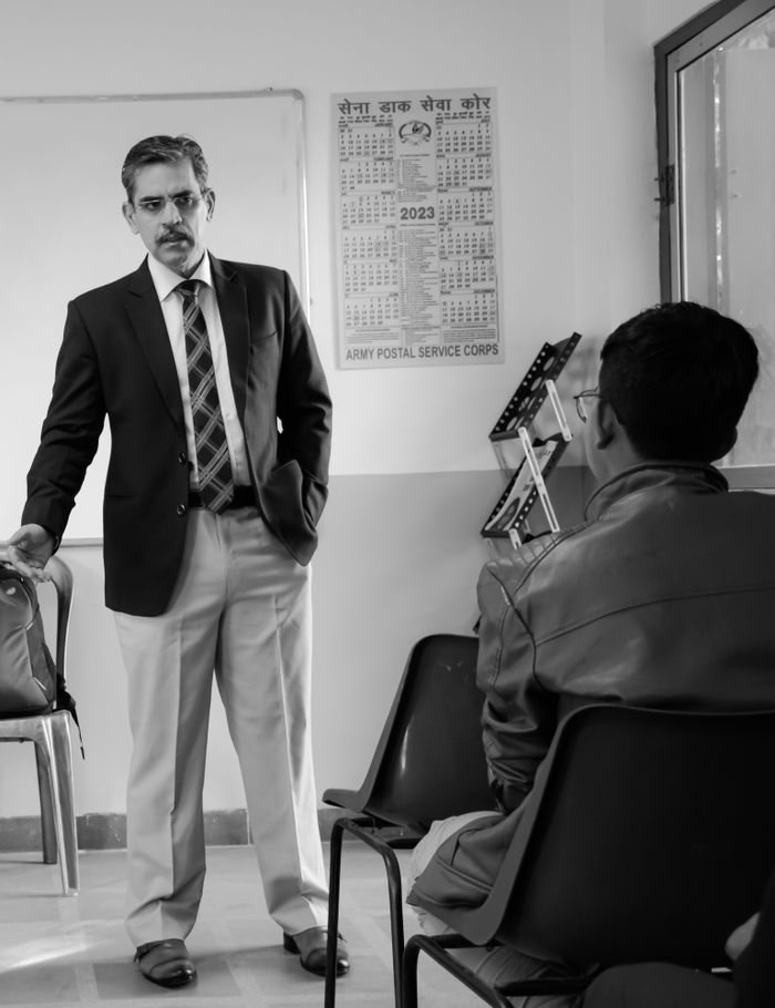 Adult man in a black blazer giving a presentation to attendees in a classroom setting.